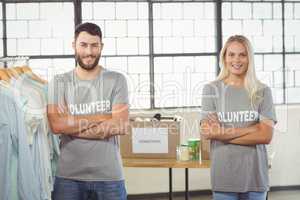 Portrait of volunteers with arms crossed standing by clothes rac