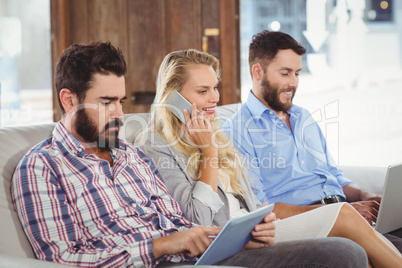 Woman talking over phone while colleagues using technologies