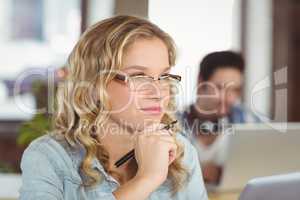 Thoughtful woman with hand on chin while colleagues working in b