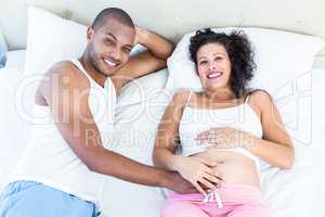 Portrait of pregnant wife with husband lying on bed