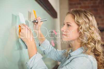 Beautiful woman holding sticky note while writing on glass board