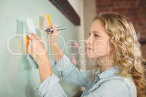 Beautiful woman holding sticky note while writing on glass board