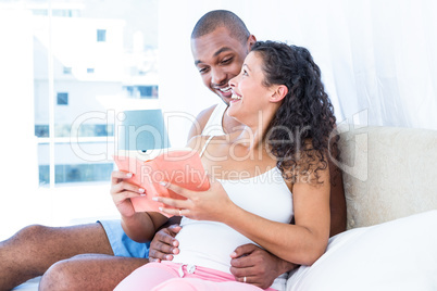 Happy pregnant wife with husband reading book at home