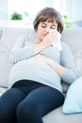 Pregnant woman sitting on a sofa about to sneeze