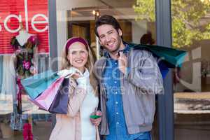 Smiling couple with shopping bags in front of window