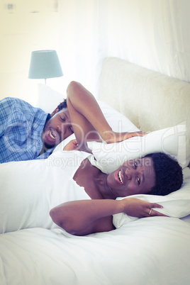 Woman covering ears with pillow while her husband is snoring