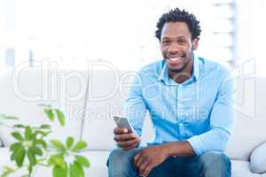 Portrait of smiling man holding smartphone at home