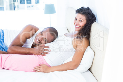 Portrait of man listening to belly of pregnant wife on bed