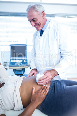 Smiling male doctor performing ultrasound on pregnant woman