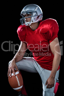 Sportsman holding American football while kneeling