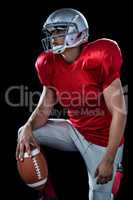 Sportsman holding American football while kneeling