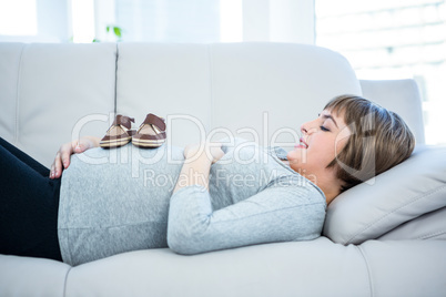 Smiling pregnant woman with baby shoes on belly