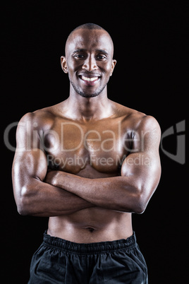 Portrait of happy shirtless athlete standing with arms crossed