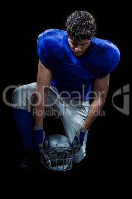 American football player looking down while holding helmet