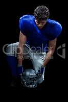 American football player looking down while holding helmet