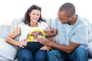 Cheerful man with headphones on pregnant belly