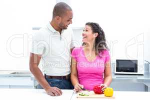 Happy pregnant wife looking at husband while chopping vegetablea