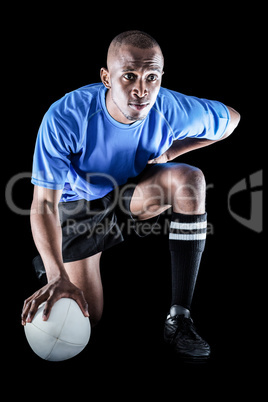 Serious rugby player kneeling while holding ball