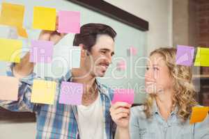 Smiling business people touching sticky notes on glass in office