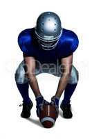 American football player in uniform holding ball while crouching