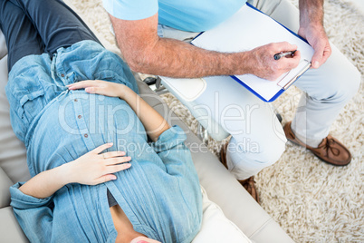 Gynaecologist writing on clipboard by pregnant woman lying on so