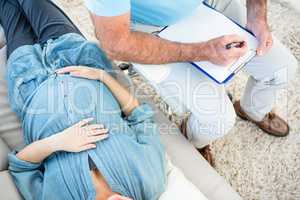 Gynaecologist writing on clipboard by pregnant woman lying on so