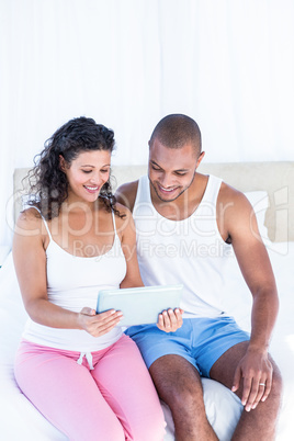 Happy husband with pregnant wife holding digital tablet