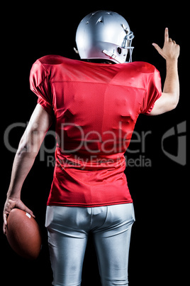 Rear view of American football player pointing while holding bal