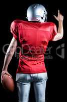 Rear view of American football player pointing while holding bal
