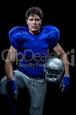 Portrait of serious sportsman with hand on knee holding helmet