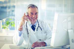 Portrait of smiling male doctor using telephone in clinic