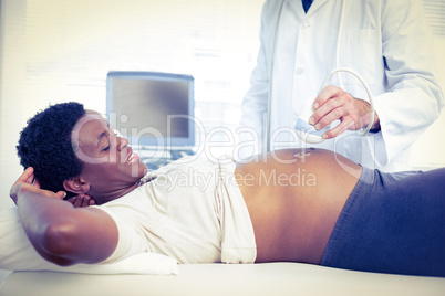 Male doctor performing ultrasound on smiling pregnant woman