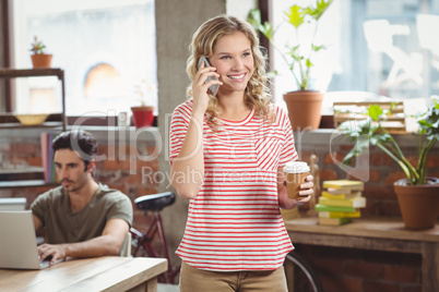 Happy businesswoman talking over phone while holding coffee in o