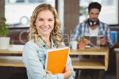 Portrait of smiling woman holding spiral notebook in office