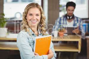 Portrait of smiling woman holding spiral notebook in office