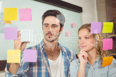 Woman looking at colleague wiriting on sticky notes attached on