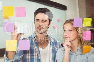 Woman looking at colleague wiriting on sticky notes attached on