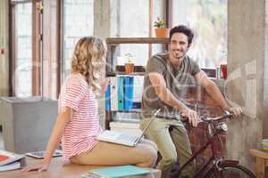 Man with bicycle discussing with colleague in office