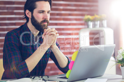 Focused editor with hand clasped using laptop