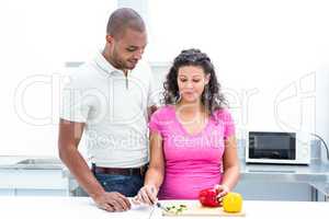 Pregnant wife chopping vegetable while husband looking at her