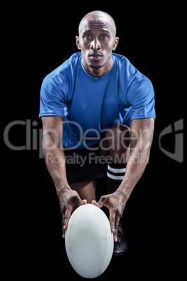 Portrait of rugby player holding ball while kneeling