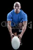 Portrait of rugby player holding ball while kneeling