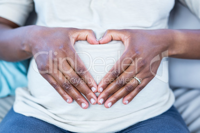 Mid section of woman making heart shape on her belly