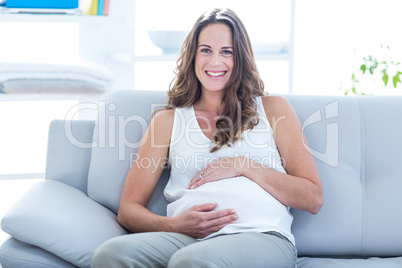 Smiling pregnant woman sitting with hand on stomach on sofa