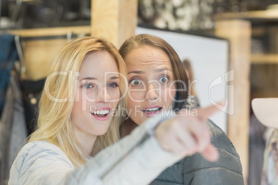 Two astonished female friends pointing away