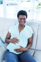 Portrait of smiling pregnant woman touching belly while sitting