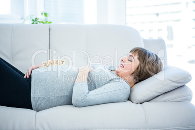 Pregnant woman playing with wooden blocks while lying on a sofa