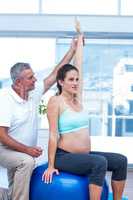 Instructor assisting pregnant woman sitting on ball