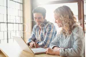 Happy colleagues looking at laptop in creative office