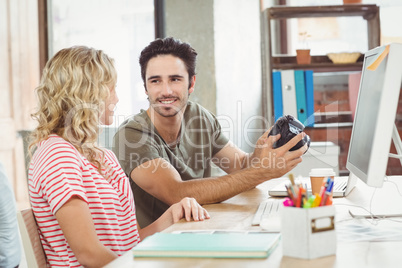 Businessman holding digital camera while discussing with colleag